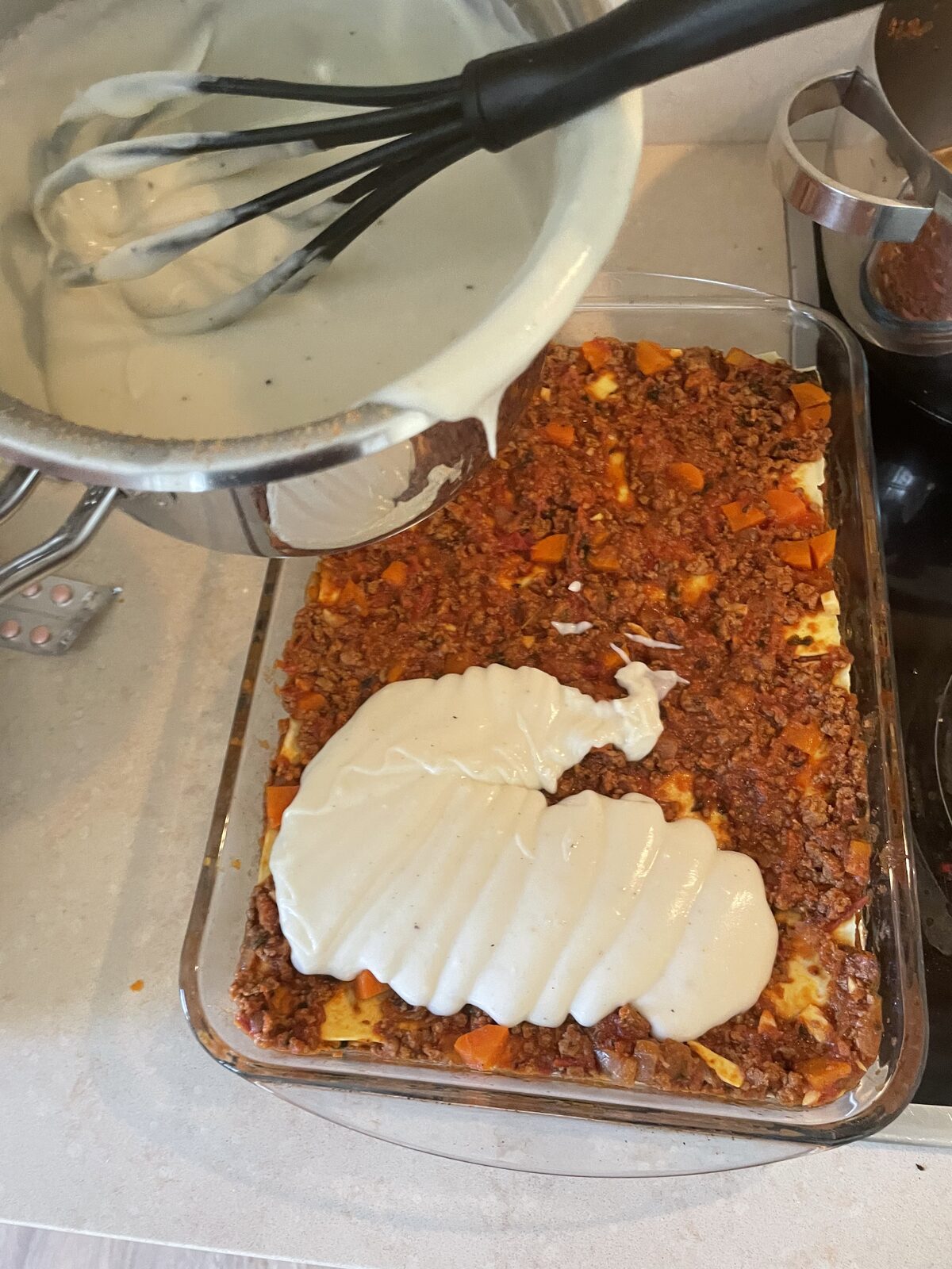 Béchamel being poured over the final ragù layer