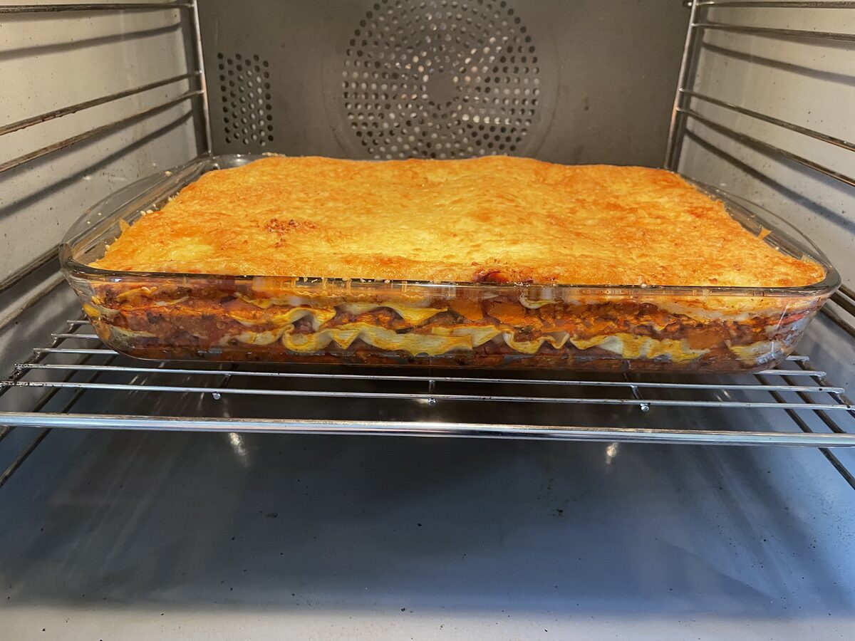 The finished lasagna, golden brown on top with visible layers through the glass